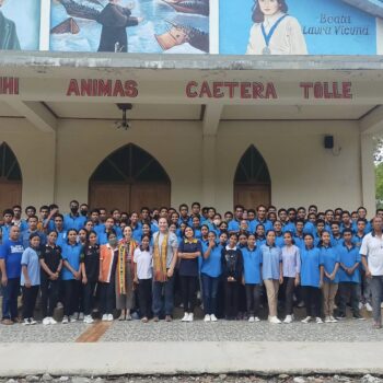 Grupo de jovens estudantes e educadores reunidos em frente a uma escola em Timor-Leste, representando as atividades educativas e recreativas promovidas pela GiraCatavento para incentivar a aprendizagem da língua portuguesa.